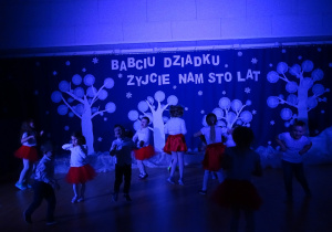 Żabki tańczą do piosenki "Chu chu ua" na na sali gimnastycznej w świetle kolorowych reflektorów.